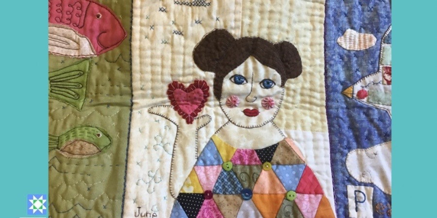 Que Son Las Quilts De Arte - Quilt de una mujer de frente con vestido de triangulos de tela en varios colores sosteniendo en su mano un corazon